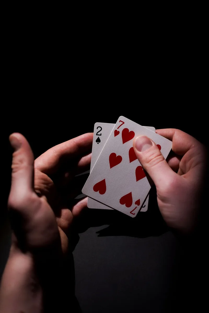 Hands holding two playing cards against a dark background